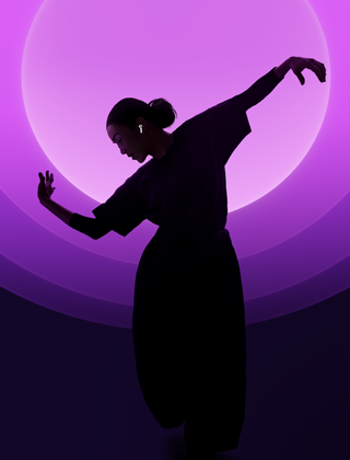 Una persona baila con unos AirPods 5 puestos, fondo multicolor