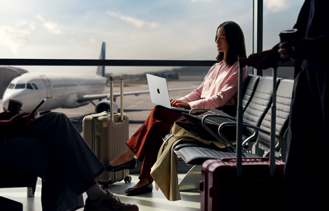 Una persona escribe en una MacBook Pro de 14 pulgadas color plata que no está enchufada, mientras espera su vuelo en la sala de abordaje