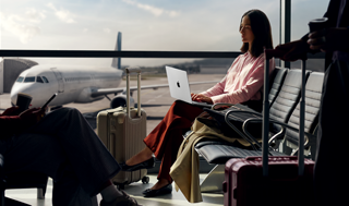 Una persona escribe en una MacBook Pro de 14 pulgadas color plata que no está enchufada, mientras espera su vuelo en la sala de abordaje