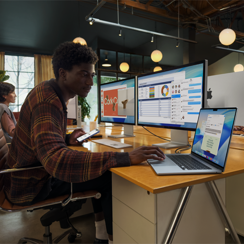 Una persona sentada en un escritorio trabaja con dos monitores Studio Display mientras usa una MacBook Air de 15 pulgadas, y los monitores muestran ventanas de Keynote, Vista Previa, Excel, Mensajes y Mail