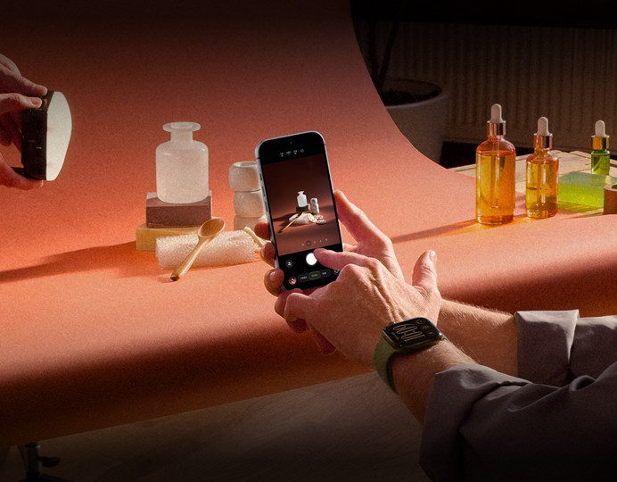 Una sesión de fotos en un lugar de trabajo, una persona usa un iPhone para fotografiar productos sobre un fondo, otra persona sostiene un foco