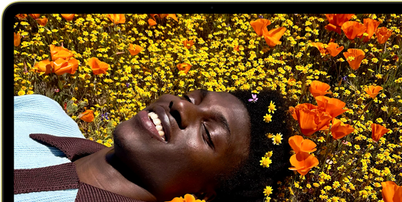 MacBook Neo, color amarillo cítrico, la pantalla muestra a una persona sonriente acostada en un campo de flores bajo el sol