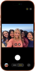 iPhone 17 Pro en naranja cósmico, frente, la pantalla muestra la cámara frontal Center Stage abierta con una selfie grupal de cinco personas centradas en el encuadre